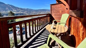 Une terrasse en bois avec une table et des chaises, offrant une vue sur un paysage montagneux.