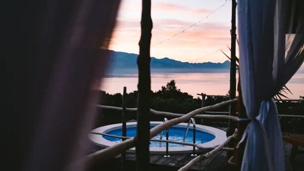 Banheira de hidromassagem com vista para um lago e montanhas ao pôr do sol.
