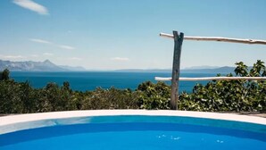 Uma piscina azul cristalina com vista para o mar e montanhas ao fundo.