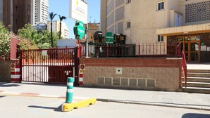 A gated entrance with a red metal gate, a brick wall, and a green and white bollard. - La Oca 9-2 (Benidorm)