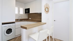 A modern kitchen with a built-in washing machine, a wooden countertop, and a white chair. - La Oca 9-2 (Benidorm)
