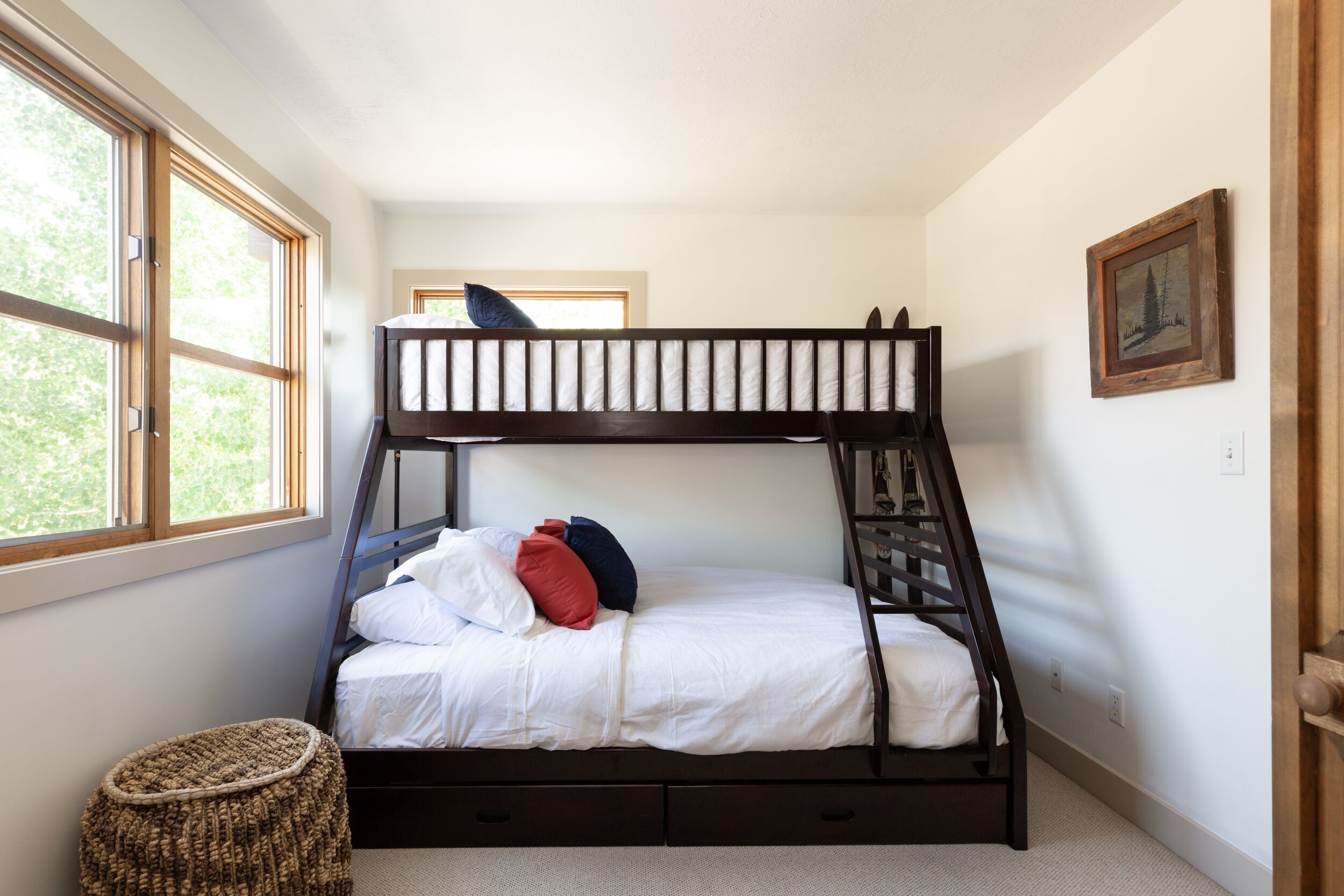 Een stapelbed met een houten frame, witte beddengoed en een klein geweven krukje.