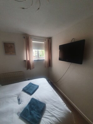 Une chambre d’hôtel avec un lit, un téléviseur fixé au mur, une fenêtre avec des rideaux et un radiateur.
