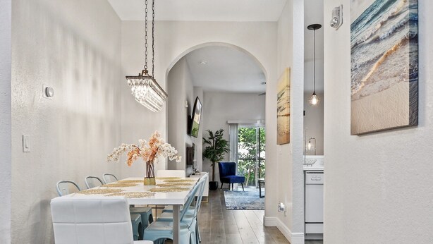 A dining area with a long table, white chairs, and a chandelier. There is a painting on the wall and a plant in the background. - Chic Disney Condo/w Fireplace at Bahama Bay Resort 15 mins from Disney  (Davenport)