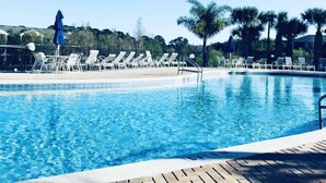 A clear blue pool with lounge chairs and umbrellas, surrounded by palm trees and a fence. - Chic Disney Condo/w Fireplace at Bahama Bay Resort 15 mins from Disney  (Davenport)