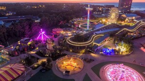 Vue aérienne d’un parc d’attractions au crépuscule, avec des manèges et des structures illuminés.