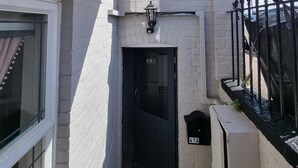 Une ruelle étroite avec une porte noire, une boîte aux lettres portant l’inscription « 47A », et un mur de briques blanches.