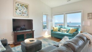 Ein Wohnzimmer mit einem großen Flachbildfernseher, einem blaugrünen Sofa und einem braunen Ledersessel.