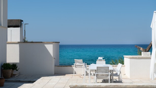 Terraço com mobiliário branco com vista para o mar.