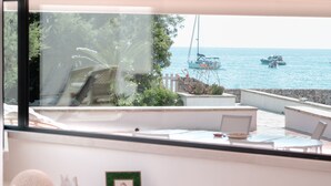 Uma varanda com vista para o mar, com guarda-corpo branco, uma mesa pequena e uma cadeira.