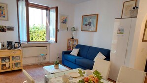 Una sala de estar acogedora con un sofá azul, una mesa de comedor dispuesta con platos y un bol, y una ventana con cortinas.