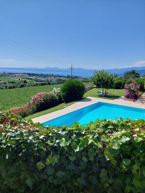 A swimming pool surrounded by lush greenery and a scenic view of a lake and mountains. - Regarda - Nido dell'Arte, apartment in Bardolino with pool and lake view (Bardolino)