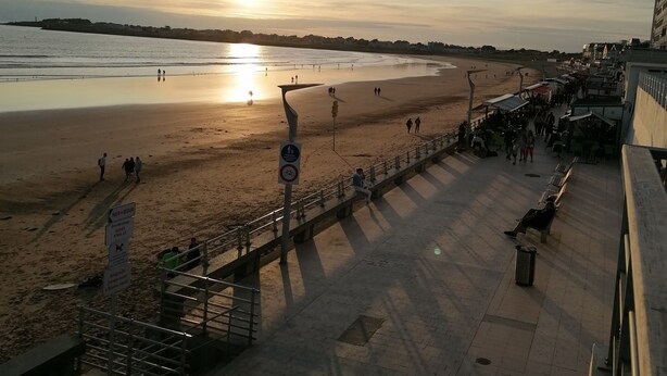 Una playa con un atardecer, un paseo marítimo y algunas personas caminando.