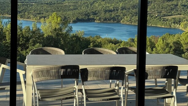Une terrasse avec une table et des chaises donnant sur un lac et des collines boisées.