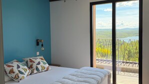 Une chambre à coucher avec un lit, un ventilateur de plafond, une fenêtre donnant sur un paysage verdoyant et un balcon.