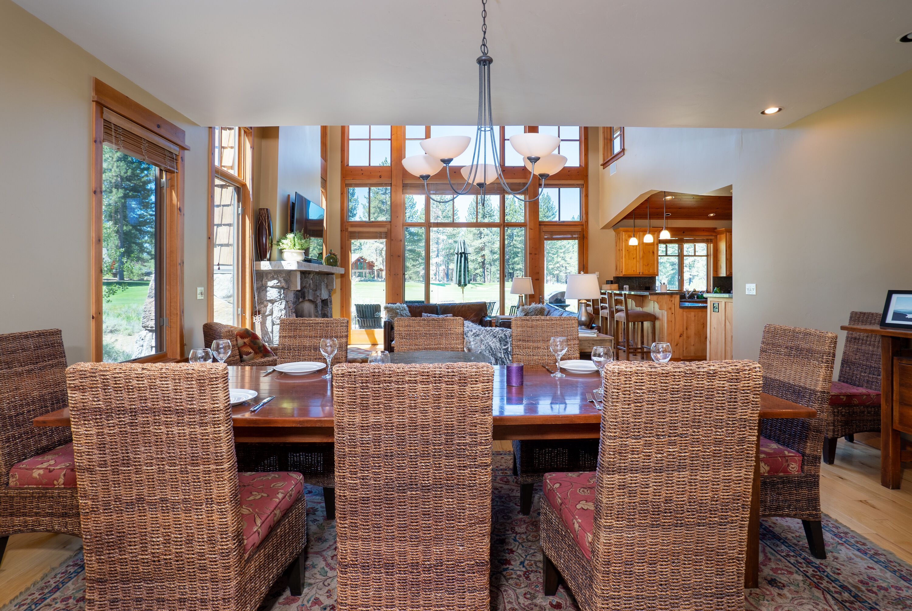 Un coin repas avec des chaises en osier et une table en bois, de grandes fenêtres et une cuisine en arrière-plan.
