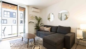 A modern living room with a grey sofa, a round coffee table, and a large window with a view of a building.