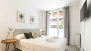 A hotel room with a large bed, a flat-screen TV, a bedside table with a lamp, and two framed leaf artworks on the wall.
