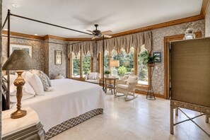 Ein geräumiges Schlafzimmer mit einem großen Bett, einem Deckenventilator und Blick ins Freie durch große Fenster.