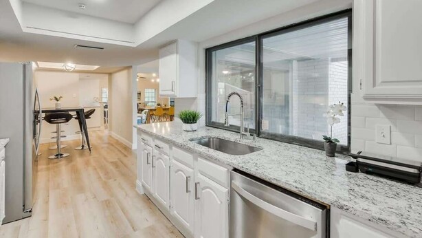 Una cocina moderna con muebles blancos, encimera de granito y un ventanal grande.