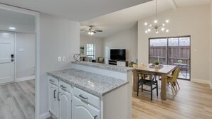 Una cocina moderna con armarios blancos, encimera de granito y una zona de comedor con mobiliario de madera.
