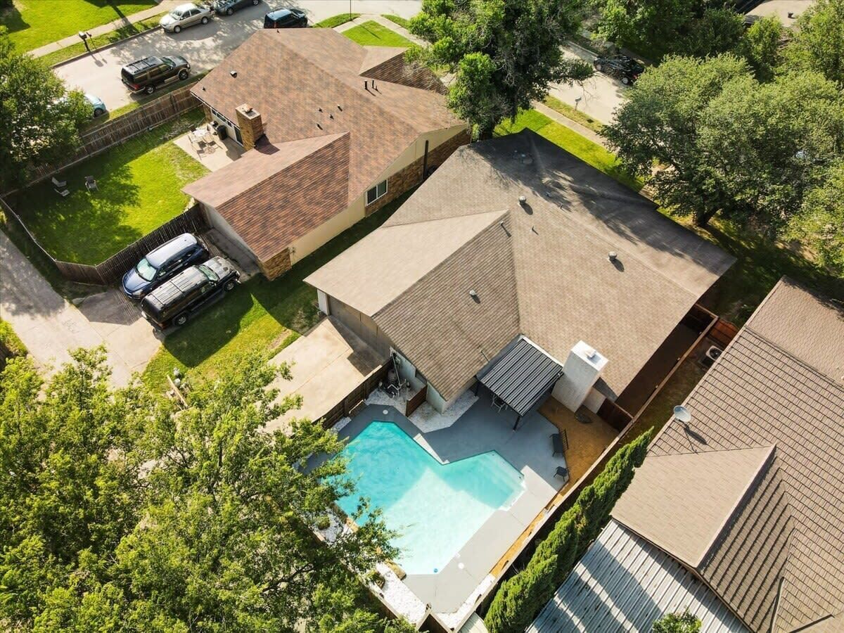 A residential property with a swimming pool, a covered patio, and a fenced driveway.