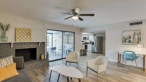 Una sala de estar moderna con chimenea, ventilador de techo y vista a la cocina.