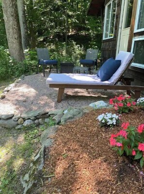 Relax in a serene outdoor space with a lounge chair and small table, surrounded by lush greenery and vibrant flowers.