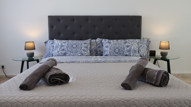 A neatly made bed with rolled towels, a dark headboard, patterned pillows, and two bedside lamps on glass tables. - Your central and comfortable 100 sqm flat in Valencia City. 10 Gigabit internet (Valencia)