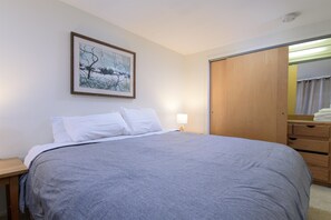 A neatly made bed with a gray blanket, a bedside lamp, and a framed picture on the wall. - 208 Village Gate Studio Bedroom Condo by RedAwning (Warren)