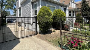 A two-story house with a garage, a gated driveway, and a well-maintained garden with flowers.