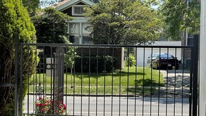 A gated driveway leading to a house with a garage, surrounded by greenery and a parked car.