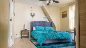 A bedroom with a bed, a nightstand, a ceiling fan, and a window with curtains.