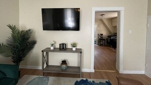 A living room with a flat-screen TV mounted on the wall, a coffee table, a sofa, and a potted plant.
