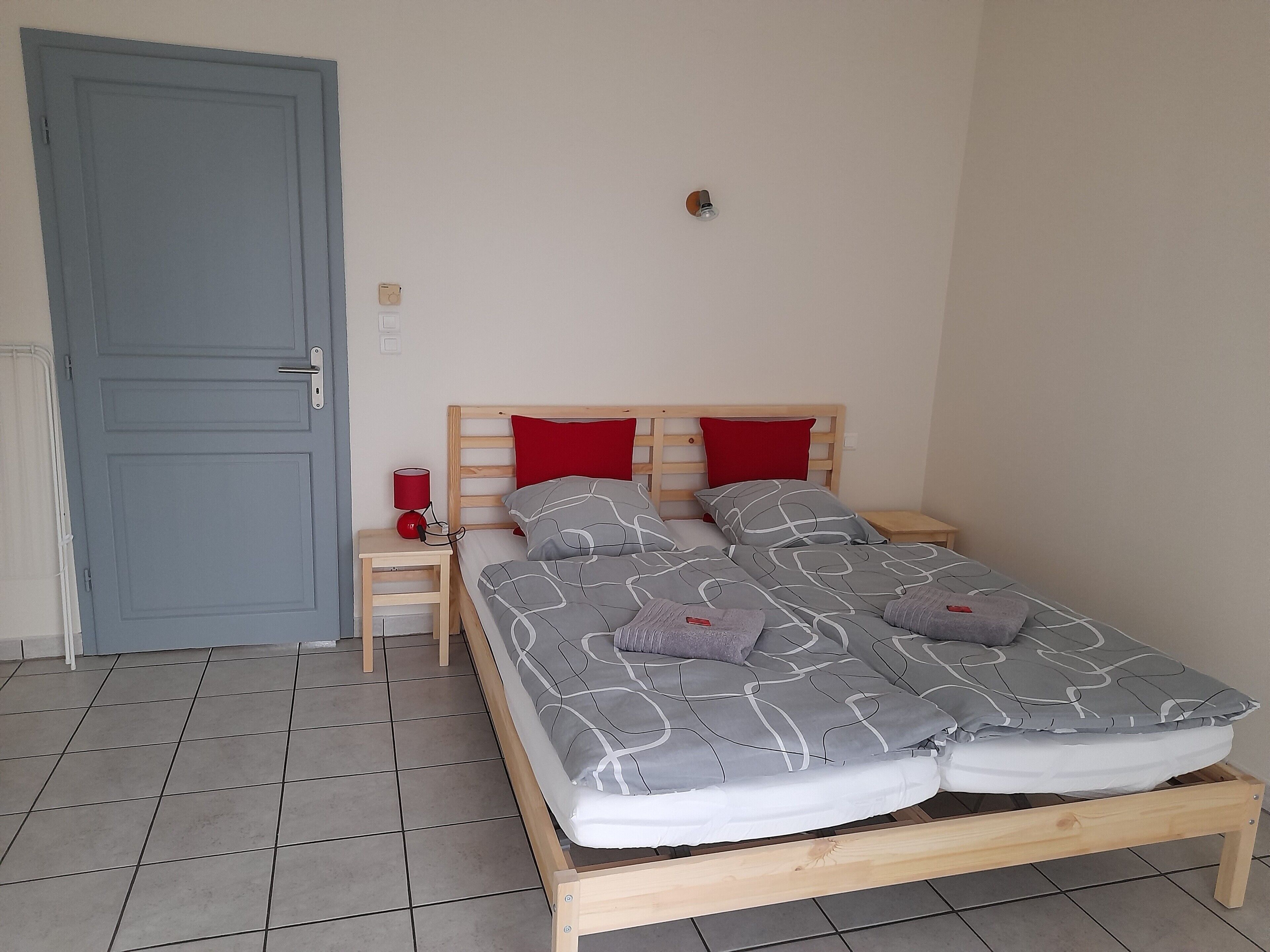 Een kamer met een bed, een nachtkastje, een rode lamp en een blauwe deur.