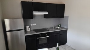 Uma cozinha compacta com forno embutido, geladeira de aço inoxidável, pia e armários pretos.