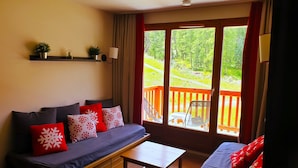 A cozy living room with a sofa, a wooden coffee table, and a view of a wooden deck and greenery outside. - Résidence Lalbane - Piscine - Vars Les Claux (Vars)