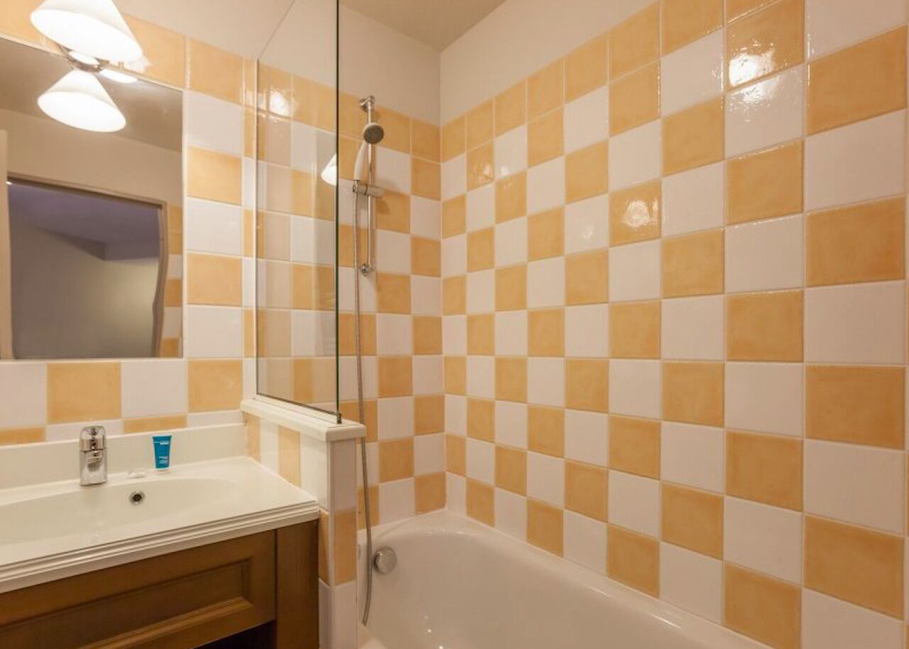 A bathroom with a checkered tile wall, a white bathtub, and a mirror above the sink.
