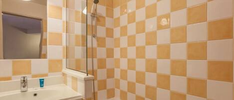 A bathroom with a checkered tile wall, a white bathtub, and a mirror above the sink.