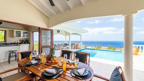 A dining area with a view of the ocean, a kitchen, and a pool.