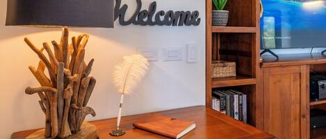 Un escritorio de madera con una lámpara, un letrero de bienvenida y un televisor al fondo.
