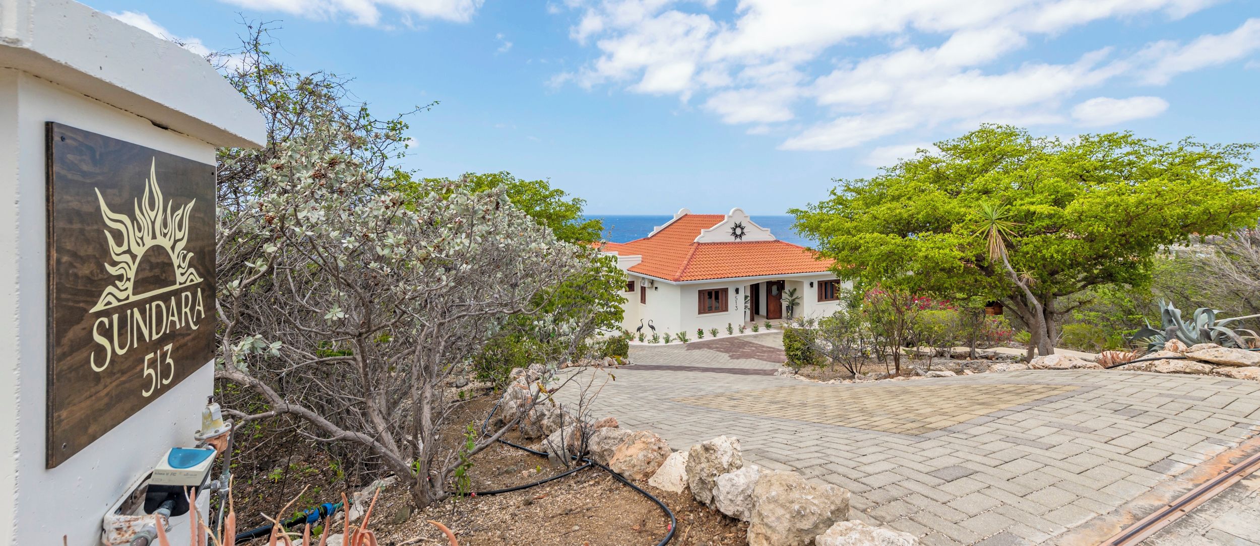 A coastal property with a sign reading 'SUNDARA 513', a paved driveway, and a building with a red-tiled roof.