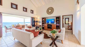 A spacious living room with a large TV, comfortable seating, and a view of the ocean.