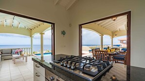 A kitchen with a gas stove, a digital clock, and a view of the ocean through an open door. - Villa Azure Rose - Coral Estate (Curaçao)