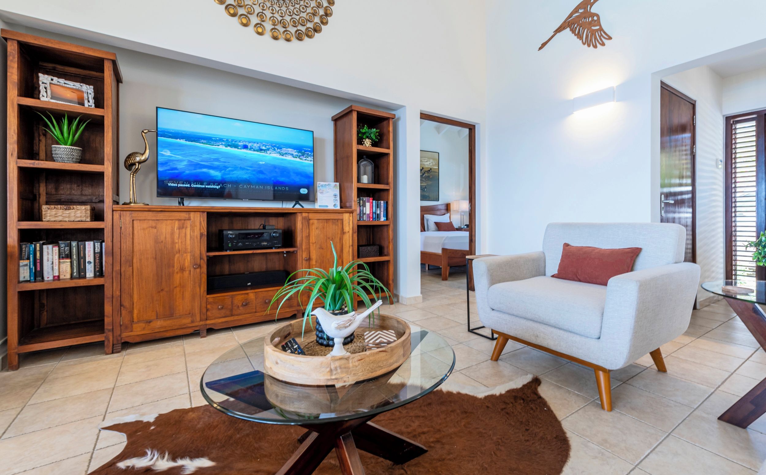 A living room with a flat-screen TV, wooden bookshelves, a glass coffee table, a sofa, and a cowhide rug.