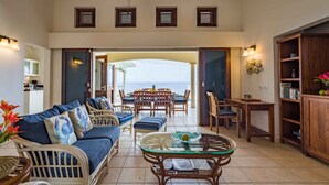 A spacious living area with a sofa set, a glass coffee table, and a view of the ocean. - Villa Azure Rose - Coral Estate (Curaçao)