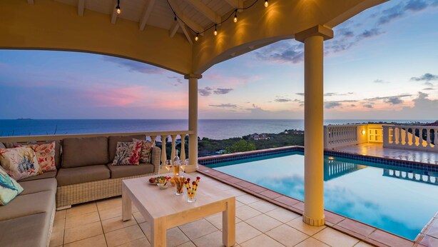 A covered outdoor seating area with a pool, a view of the sea, and a sunset. - Villa Azure Rose - Coral Estate (Curaçao)