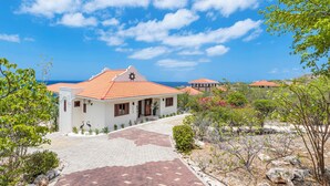 A coastal property with a paved entrance, a white building with a red-tiled roof, and a view of the sea.