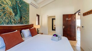 Ein Hotelzimmer mit einem großen Bett, einem Pfau-Gemälde, einer Holztür mit der Aufschrift 'Peacock' und Blick ins Freie.