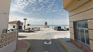 En gatubild med en strand i bakgrunden, en livräddartorn och en skylt med texten ”Parkering förbjuden”.